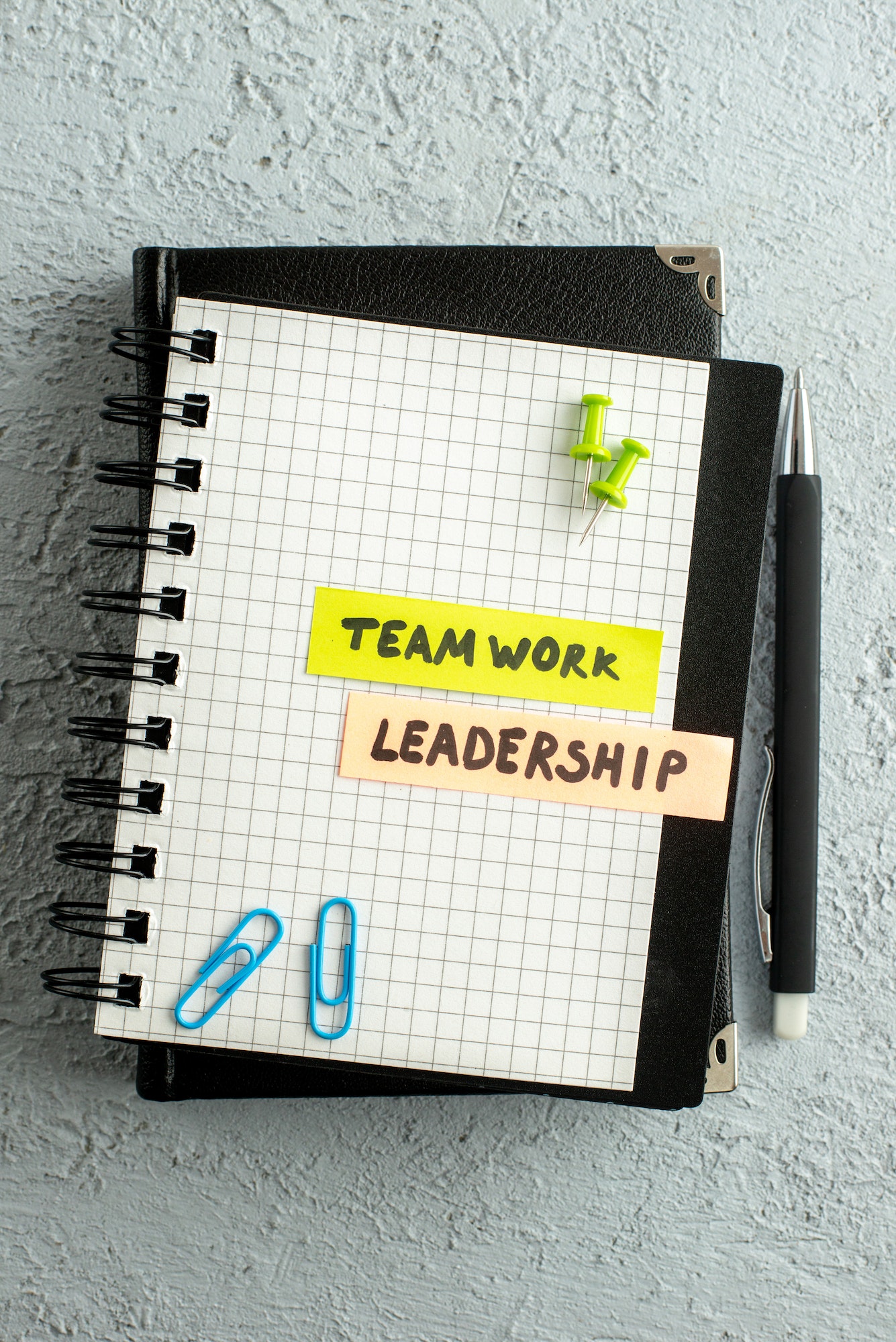 Vertical view of TEAMWORK LEADERSHIP writings on coloured sheets on spiral notebook and book on